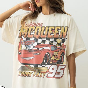 K&ouml;nnte beinhalten: Elfenbeinfarbenes T-Shirt mit einem Aufdruck von Lightning McQueen aus dem Film Cars. Das Design enth&auml;lt den Text "Lightning McQueen", "Cars", "95" und "Think Fast". Das Shirt hat kurze &Auml;rmel und eine lockere Passform.