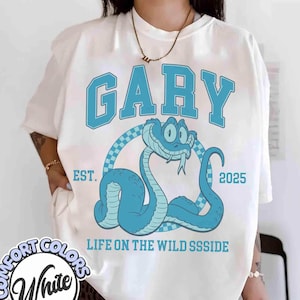May include: White Comfort Colors t-shirt with a blue snake graphic. The word "GARY" is arched above the snake, with "EST. 2025" and "LIFE ON THE WILD SSSSIDE" below. The snake is inside a checkered circle.