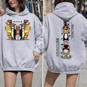 May include: Sport grey hoodie featuring colorful cartoon characters on the front and back. The front design includes smiling cat-like creatures and other characters. The back displays a vertical stack of animated figures with "STUDIO GHIBLI" text.