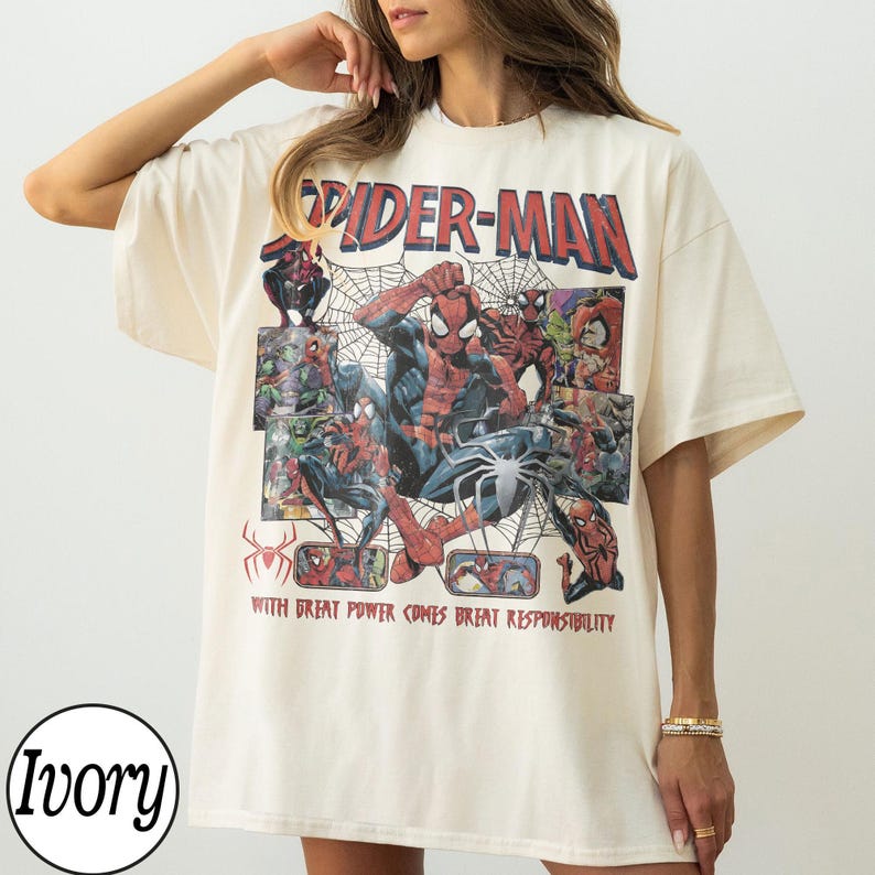 May include: Ivory-colored t-shirt featuring a Spider-Man graphic. The design includes the words "Spider-Man" in red, along with comic book illustrations of the superhero. The text "WITH GREAT POWER COMES GREAT RESPONSIBILITY" is also present.