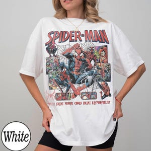May include: White t-shirt featuring a Spider-Man graphic. The design includes the words "SPIDER-MAN" in red and images of Spider-Man in action, along with the phrase "WITH GREAT POWER COMES GREAT RESPONSIBILITY."