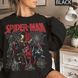 Pu&ograve; includere: Felpa nera con grafica di Spider-Man. Il design include la scritta "SPIDER-MAN" in rosso, con immagini di Spider-Man e altri personaggi, insieme a ragnatele. La parola "BLACK" &egrave; nell'angolo in alto a destra.