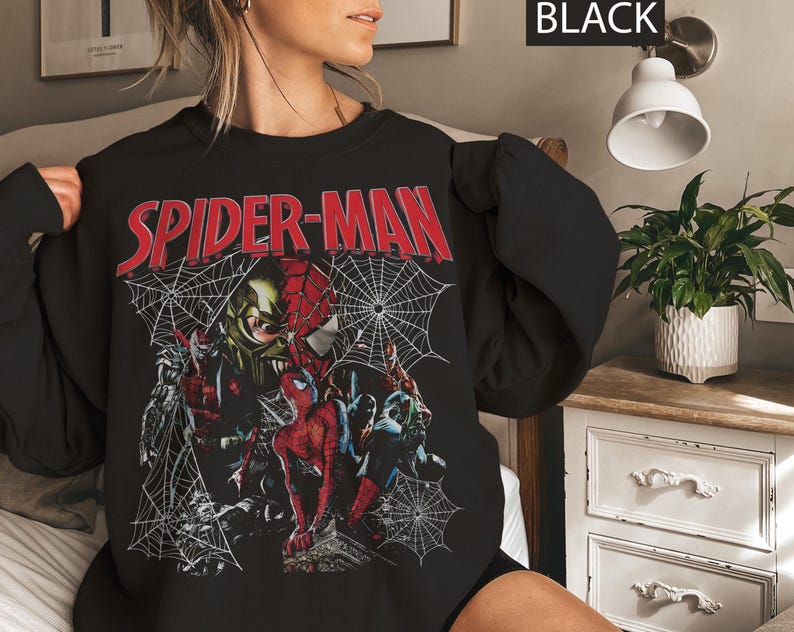Pu&ograve; includere: Felpa nera con grafica di Spider-Man. Il design include la scritta "SPIDER-MAN" in rosso, con immagini di Spider-Man e altri personaggi, insieme a ragnatele. La parola "BLACK" &egrave; nell'angolo in alto a destra.