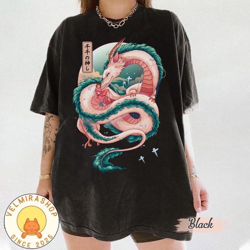 May include: Black t-shirt featuring a detailed illustration of a dragon with a pink and white body, teal accents, and Japanese text. The dragon is set against a backdrop of a moon and clouds. The shirt has a vintage wash.