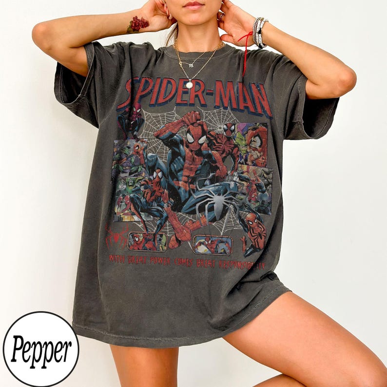 May include: Dark gray Spider-Man graphic t-shirt. The shirt features a collage of Spider-Man illustrations, the words "SPIDER-MAN" in red, and a spider web design. The shirt is a casual, oversized fit.