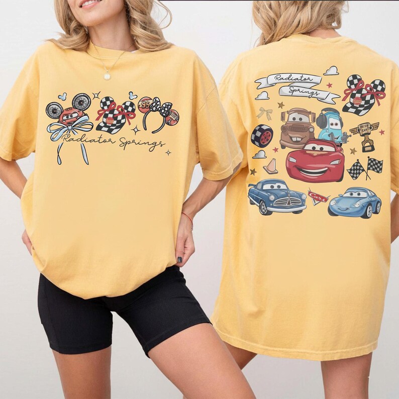 May include: Yellow t-shirt featuring a front graphic of Mickey Mouse ears, checkered patterns, and the text "Radiator Springs." The back of the shirt displays various car illustrations and the words "Radiator Springs" in a banner.