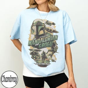 May include: Light blue t-shirt featuring a graphic from "The Mandalorian and Grogu." The design includes the Mandalorian's helmet, Grogu, and the text "This is the Way." The shirt is a relaxed fit.