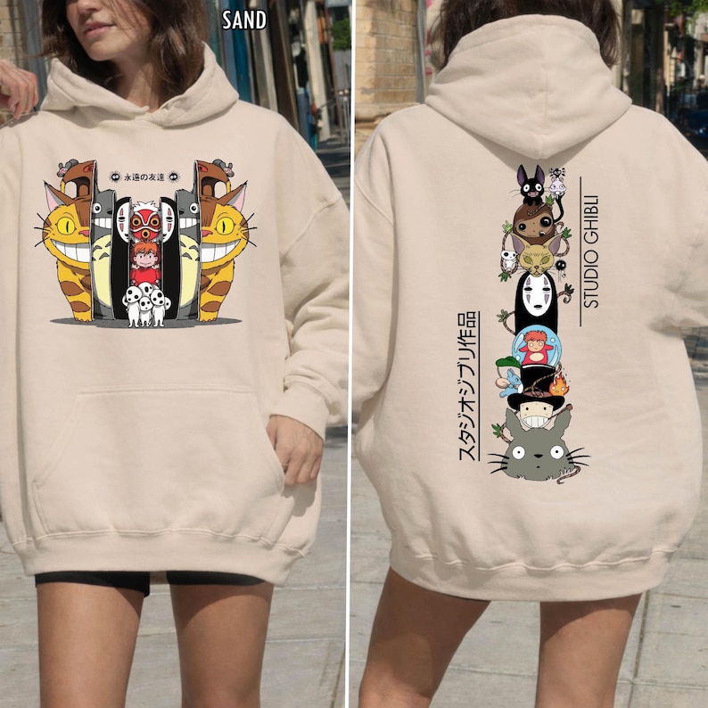 May include: Sand-colored hoodie featuring a front graphic of animated characters and Japanese text. The back displays a vertical stack of characters with "STUDIO GHIBLI" and Japanese text. The hoodie has a hood and a front pocket.
