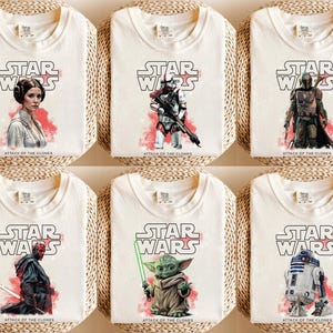 May include: Six cream-colored t-shirts featuring Star Wars characters and the text "STAR WARS" in a bold font. Each shirt displays a different character illustration with the text "ATTACK OF THE CLONES". The shirts are arranged on woven mats.