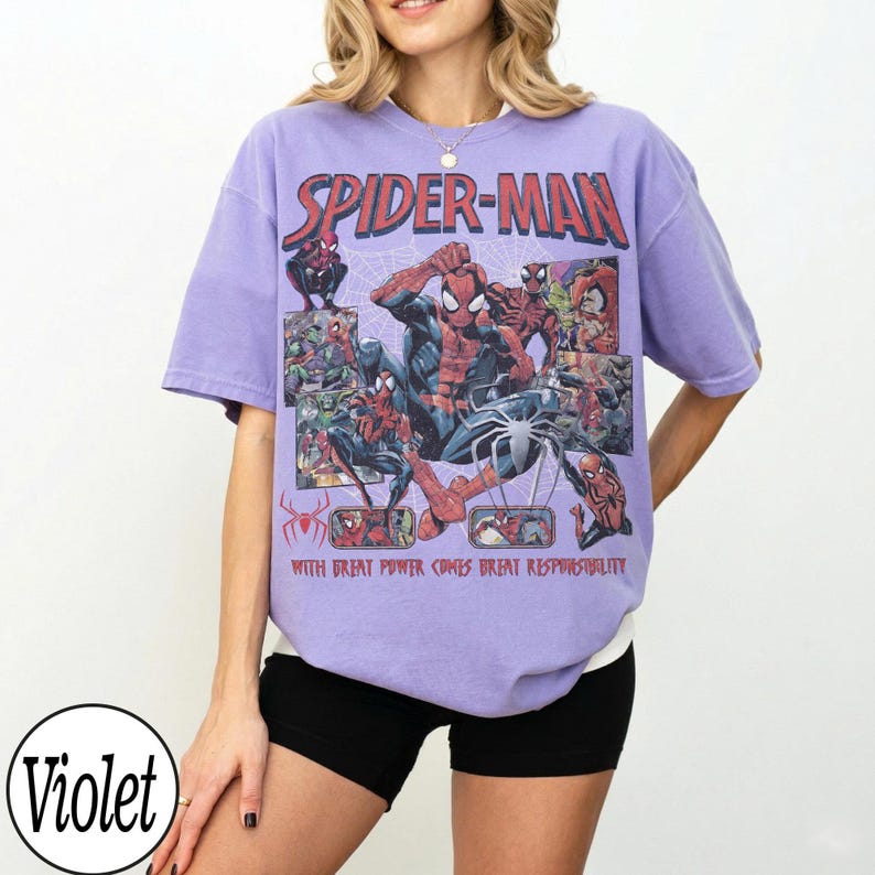 May include: A violet-colored t-shirt featuring a Spider-Man graphic. The graphic includes the words "Spider-Man" and the phrase "With great power comes great responsibility." The design showcases various Spider-Man illustrations.