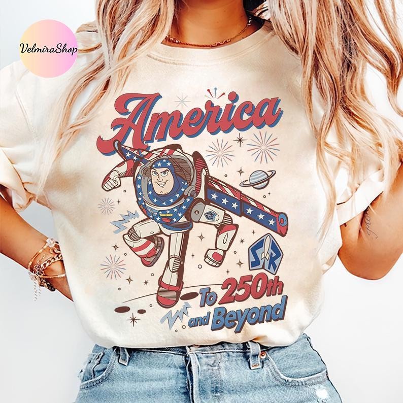 May include: Cream-colored t-shirt featuring a cartoon illustration of a space ranger in patriotic colors. The design includes the word "America" in red and blue script, with the text "To 250th and Beyond" below.