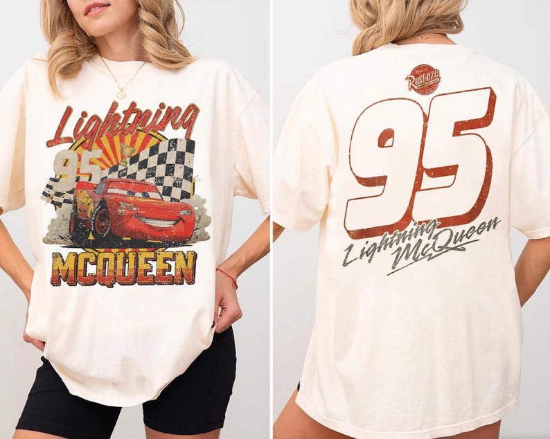 May include: An off-white t-shirt featuring a graphic of a red race car with the text Lightning 95 MCQUEEN on the front. The back of the shirt displays the number 95 in large white font with a red outline, the text Lightning McQueen, and a Rust-eze logo.