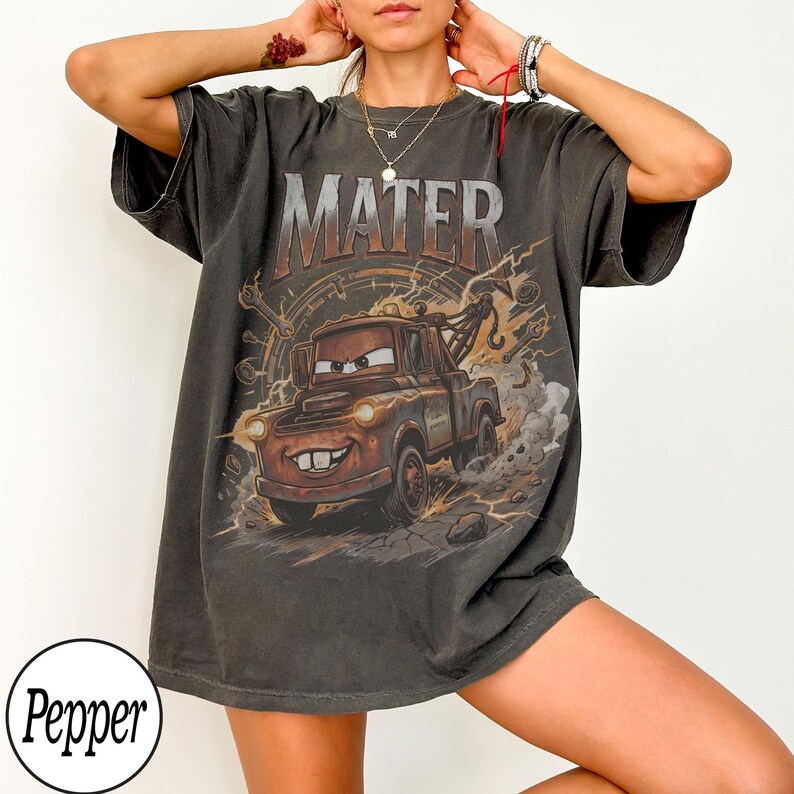 May include: Dark gray t-shirt featuring a graphic of Mater from the movie Cars. The word "MATER" is printed above the character. The design includes a brown tow truck with a smiling face, set against a background of gears and lightning.
