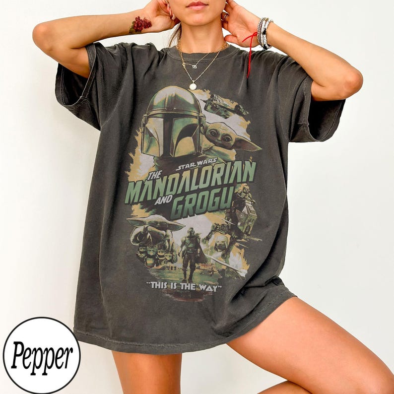 May include: Dark gray t-shirt featuring a graphic from the Star Wars series, "The Mandalorian and Grogu." The design includes images of the Mandalorian, Grogu, and the text "THIS IS THE WAY."