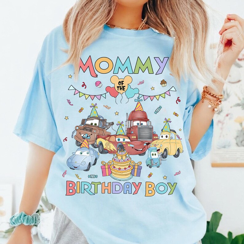 Puede incluir: Camiseta azul claro con un gr&aacute;fico colorido. El dise&ntilde;o incluye el texto "MOMMY OF THE BIRTHDAY BOY" y coches de dibujos animados, tarta de cumplea&ntilde;os, globos y confeti. La camiseta es de estilo casual.
