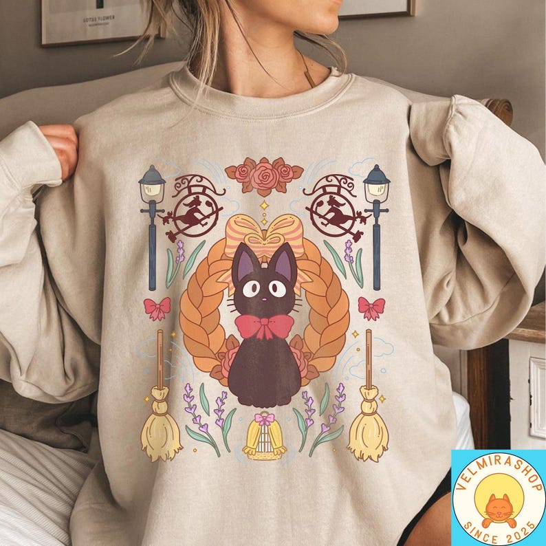 May include: Beige sweatshirt featuring a cartoon black cat with a red bow tie, surrounded by a wreath, brooms, and other decorative elements. The design includes street lamps, roses, and the text "VELMIRASHOP SINCE 2025".