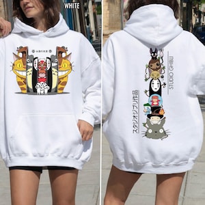 May include: White hoodie featuring a colorful graphic of animated characters on the front and back. The front graphic includes smiling cat-like creatures and other characters. The back graphic features a stack of animated characters with "STUDIO GHIBLI" text.