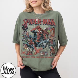 May include: Olive green Spider-Man t-shirt featuring a comic book style graphic. The design includes the words "SPIDER-MAN" in red, and the phrase "WITH GREAT POWER COMES GREAT RESPONSIBILITY".