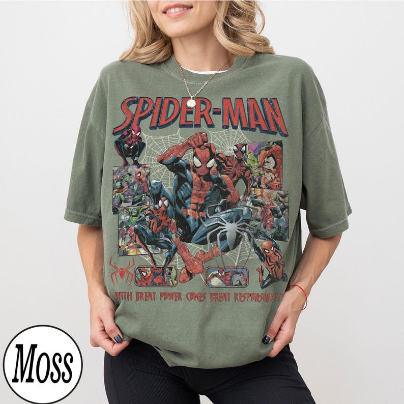 May include: Olive green Spider-Man t-shirt featuring a comic book style graphic. The design includes the words "SPIDER-MAN" in red, and the phrase "WITH GREAT POWER COMES GREAT RESPONSIBILITY".