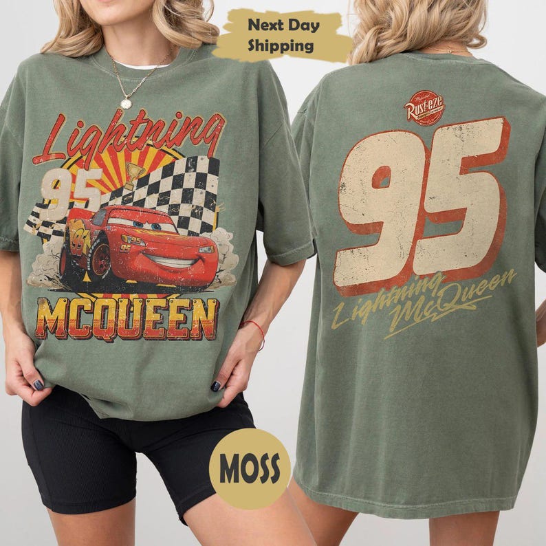 May include: An olive green t-shirt featuring a graphic of a red race car with the number 95, a checkered flag, and the text Lightning McQueen on the front. The back displays a large number 95, the text Lightning McQueen, and a Rust-eze logo.