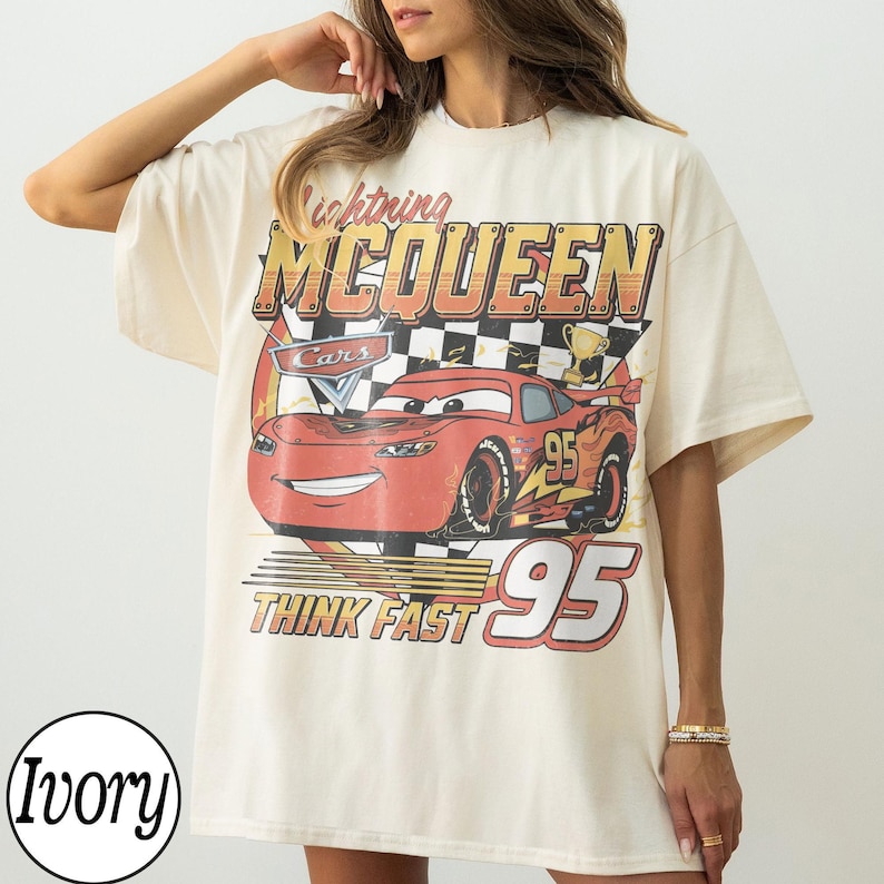 K&ouml;nnte beinhalten: Elfenbeinfarbenes T-Shirt mit einem Aufdruck von Lightning McQueen aus dem Film Cars. Das Design enth&auml;lt den Text "Lightning McQueen", "Cars", "95" und "Think Fast". Das Shirt hat kurze &Auml;rmel und eine lockere Passform.