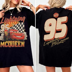 May include: A black t-shirt featuring a graphic of the red race car Lightning McQueen with the number 95, a checkered flag, and the text Lightning McQueen on the front. The back displays the large number 95 and the text Lightning McQueen.