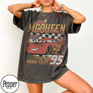 K&ouml;nnte beinhalten: Dunkelgraues T-Shirt mit Lightning McQueen aus dem Film Cars. Die Grafik zeigt McQueen, die Nummer 95 und den Text "THINK FAST". Das Shirt hat einen Vintage-Look.