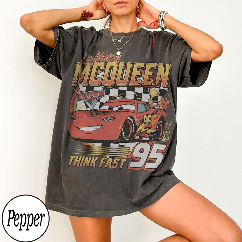 K&ouml;nnte beinhalten: Dunkelgraues T-Shirt mit Lightning McQueen aus dem Film Cars. Die Grafik zeigt McQueen, die Nummer 95 und den Text "THINK FAST". Das Shirt hat einen Vintage-Look.