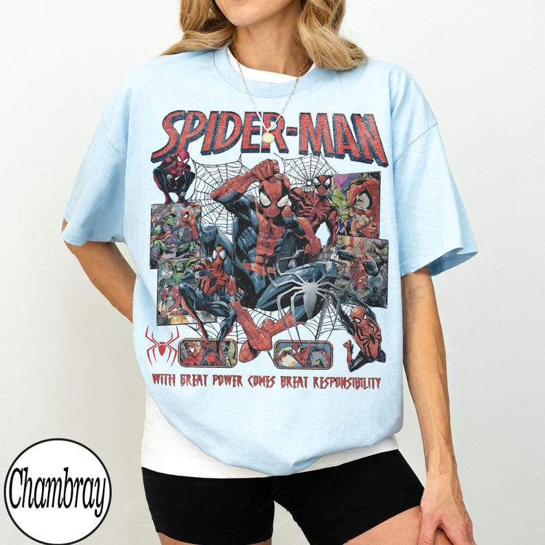 May include: Light blue t-shirt featuring a Spider-Man graphic. The design includes the words "SPIDER-MAN" in red, along with various comic book illustrations of the superhero. The text "WITH GREAT POWER COMES GREAT RESPONSIBILITY" is also present.