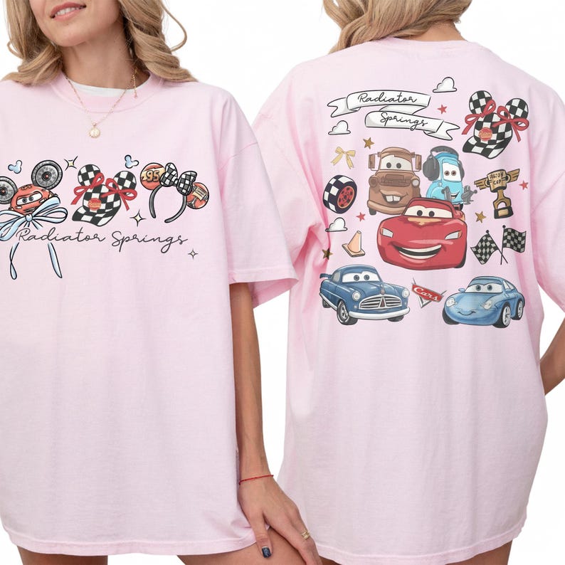 May include: A light pink t-shirt featuring a graphic of cartoon cars and mouse ears with checkered bows. The text "Radiator Springs" is also printed on the front. The back of the shirt has more car graphics and the text "Radiator Springs".