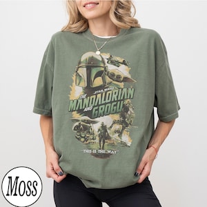 May include: Olive green t-shirt featuring a graphic from "The Mandalorian" with the text "The Mandalorian and Grogu" and "This is the Way." The design includes images of the Mandalorian and Grogu.