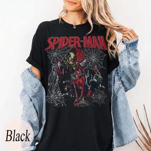 Pu&ograve; includere: T-shirt nera con la scritta rossa "SPIDER-MAN" e una grafica di Spider-Man e altri personaggi, su sfondo a ragnatela. La parola "Black" &egrave; stampata in basso.