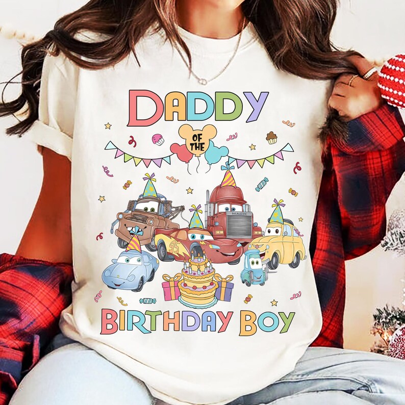 Puede incluir: Una camiseta color crema con un gr&aacute;fico colorido que dice "DADDY OF THE BIRTHDAY BOY". El gr&aacute;fico presenta coches de dibujos animados, una tarta de cumplea&ntilde;os, globos y confeti, creando un tema festivo de cumplea&ntilde;os.