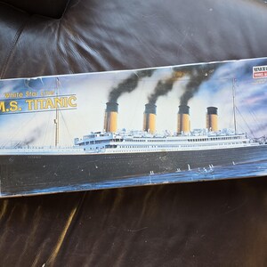 以下が含まれることがあります： Minicraft Model Kits社製R.M.S.タイタニック号モデルキットの長方形の段ボール箱。箱には、黒い煙を吐き出す4本の黄色い煙突を備えたホワイト・スター・ラインのR.M.S.タイタニック号のイラストが、青い海を背景に描かれています。