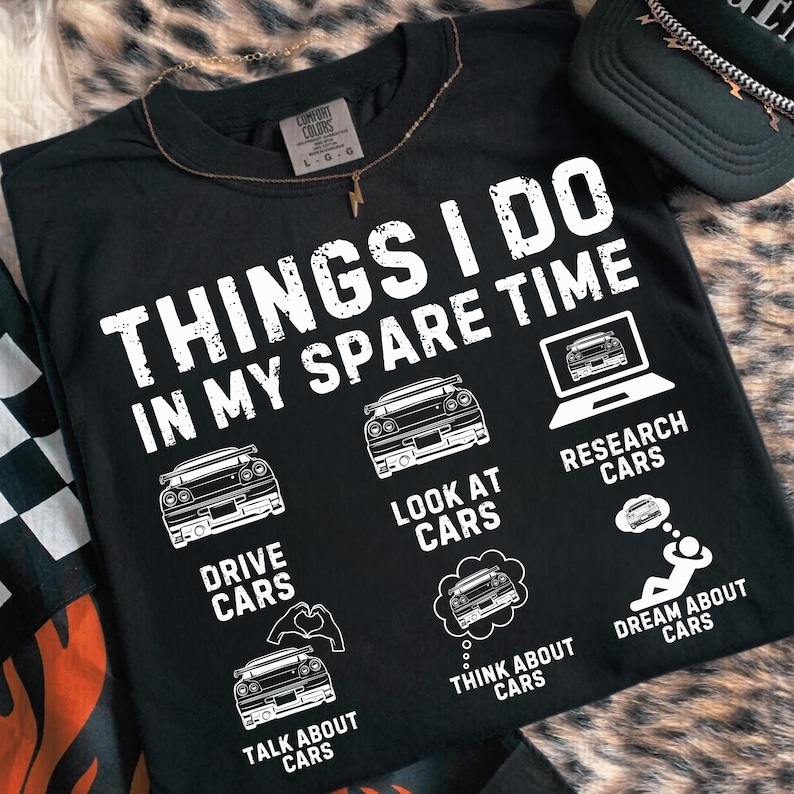 May include: Black t-shirt featuring the phrase "THINGS I DO IN MY SPARE TIME" with car-themed illustrations. The shirt includes graphics for "DRIVE CARS", "LOOK AT CARS", "RESEARCH CARS", "TALK ABOUT CARS", "THINK ABOUT CARS", and "DREAM ABOUT CARS".