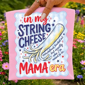 May include: A pink rectangular sign featuring a light blue striped background and a scalloped border. The text reads: in my STRING CHFESE MAMA era, with an illustration of a piece of string cheese and the phrase: overwhelmed, touched out but exactly who I'm meant to be.