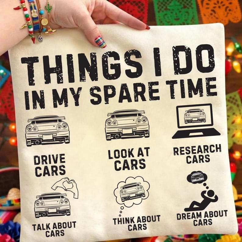 May include: Cream-coloured square cushion with the text "THINGS I DO IN MY SPARE TIME" and car illustrations. The cushion features the phrases "DRIVE CARS", "LOOK AT CARS", "RESEARCH CARS", "TALK ABOUT CARS", "THINK ABOUT CARS", and "DREAM ABOUT CARS".