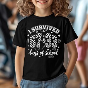 以下が含まれることがあります： 「I Survived 1+1=2 67+33 days of school」の白文字がプリントされた黒いTシャツ。デザインには星、地球儀、スクールバス、その他の学校関連のアイコンが含まれています。