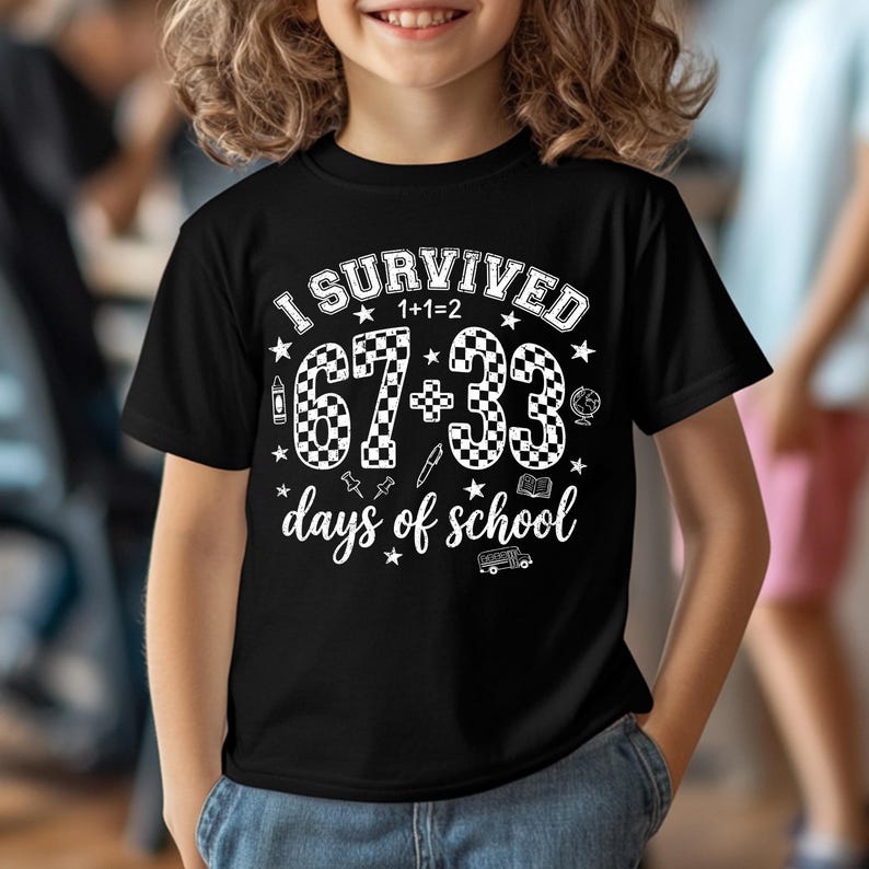 以下が含まれることがあります： 「I Survived 1+1=2 67+33 days of school」の白文字がプリントされた黒いTシャツ。デザインには星、地球儀、スクールバス、その他の学校関連のアイコンが含まれています。