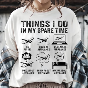 May include: White t-shirt featuring the phrase "THINGS I DO IN MY SPARE TIME" and airplane illustrations. The design includes activities such as "Go Flying," "Look at Airplanes," and "Dream About Airplanes." A humorous tee for aviation fans.