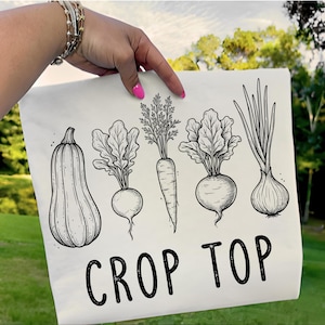 May include: White crop top featuring a black and white illustration of various vegetables, including a butternut squash, beets, carrots, and onions. The words "CROP TOP" are printed in bold, black letters below the vegetables.