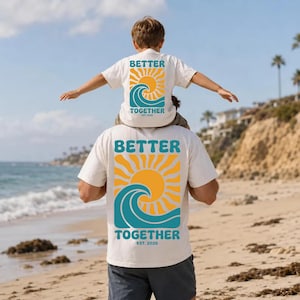 May include: Off-white short-sleeve t-shirts featuring a graphic on the back with a yellow sun, a teal ocean wave, and the text BETTER TOGETHER EST. 2026. The design is printed in a bold, retro-inspired font, centered on the back of the shirts.