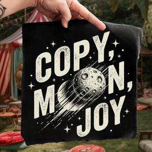 Pode incluir: Almofada quadrada preta com as palavras "COPY, MOON, JOY" em branco, juntamente com um gráfico de uma lua com um rastro. O design inclui estrelas e uma estética vintage.