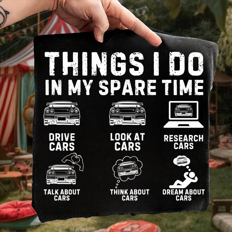 May include: Black t-shirt featuring white text and car-themed graphics. The text says "THINGS I DO IN MY SPARE TIME". Illustrations include cars, a laptop, and thought bubbles, with phrases like "DRIVE CARS", "LOOK AT CARS", "RESEARCH CARS", "TALK ABOUT CARS", "THINK ABOUT CARS", and "DREAM ABOUT CARS".