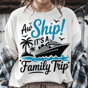 Pode incluir: Camisola branca com um gráfico azul e preto. O gráfico apresenta um navio de cruzeiro, palmeiras e o texto "Aw Ship! It's a Family Trip". O design inclui pássaros e ondas, criando um tema de férias.