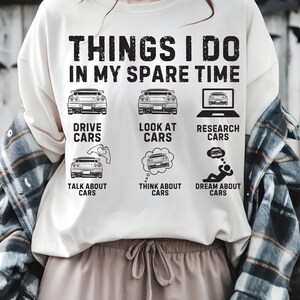May include: Cream sweatshirt featuring the text "THINGS I DO IN MY SPARE TIME" and car-themed illustrations. The design includes car images, a laptop, and speech bubbles with cars, alongside the phrases "DRIVE CARS", "LOOK AT CARS", "RESEARCH CARS", "TALK ABOUT CARS", "THINK ABOUT CARS", and "DREAM ABOUT CARS".