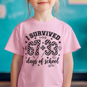 以下が含まれることがあります： 「I SURVIVED 67+33 days of school」の黒い文字がプリントされたピンク色の半袖Tシャツ。星、鉛筆、地球儀、スクールバスのグラフィックが含まれています。