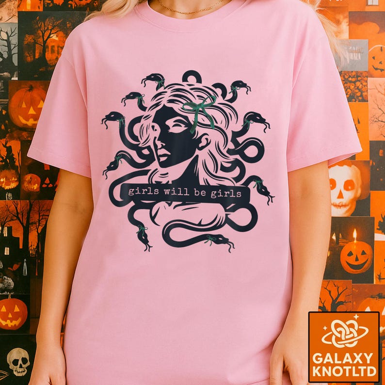 Puede incluir: Camiseta rosa claro con un gr&aacute;fico negro de Medusa y el texto "girls will be girls". El dise&ntilde;o de Medusa presenta serpientes como cabello. La camiseta tiene mangas cortas y cuello redondo.