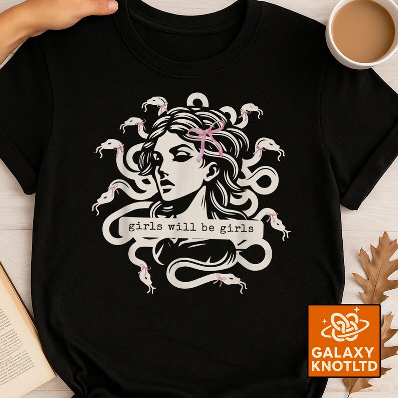 Puede incluir: Camiseta negra con una ilustraci&oacute;n blanca de una mujer con serpientes como cabello, adornada con lazos rosas. El texto "girls will be girls" se muestra en una pancarta blanca. Cuello redondo.