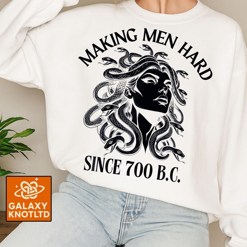 May include: White sweatshirt featuring a black graphic of Medusa with snakes for hair. The text "MAKING MEN HARD SINCE 700 B.C." is printed above and below the image. The sweatshirt has a crew neck.